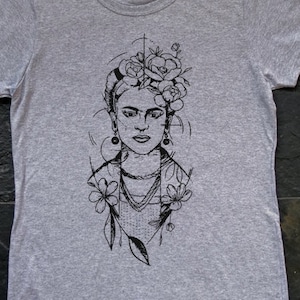 May include: A gray t-shirt with a black and white line drawing of Frida Kahlo with flowers in her hair.