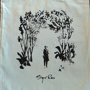 May include: Cream-colored tote bag with a black illustration of a person standing under an archway of trees. The text "Sigur Ros" is printed in black at the bottom. The bag has two cream-colored handles.