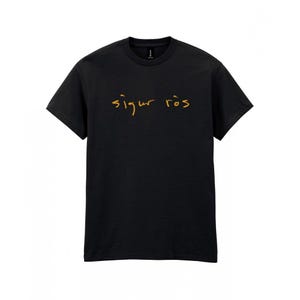 May include: Black crew neck t-shirt with the text "Sigur R&oacute;s" in gold script across the chest. The shirt is made of a soft material and has short sleeves. The text is in a handwritten style.