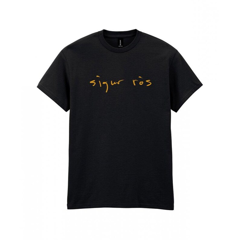 May include: Black crew neck t-shirt with the text "Sigur R&oacute;s" in gold script across the chest. The shirt is made of a soft material and has short sleeves. The text is in a handwritten style.