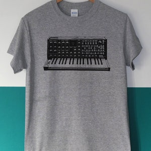 Può includere: Una maglietta grigia con una grafica in bianco e nero di una tastiera di sintetizzatore vintage. Il sintetizzatore ha la scritta "KORG" stampata su di esso.