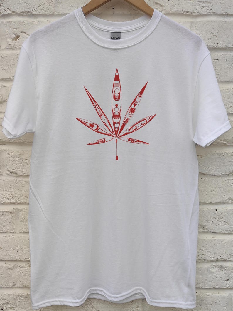 May include: White t-shirt featuring a red graphic of a cannabis leaf. The leaf design is composed of red kayak illustrations. The shirt is made of a soft, comfortable material.