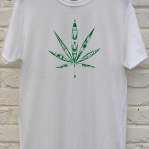 May include: White t-shirt featuring a green graphic of a cannabis leaf. The leaf design is filled with kayak illustrations. The shirt is made of a soft material and has a crew neck.