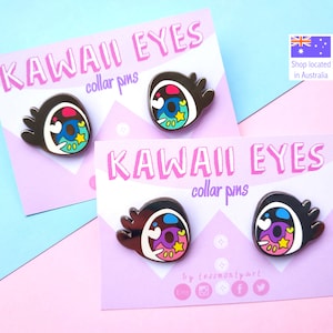 May include: Two sets of Kawaii Eyes collar pins. Each pin features a brown eye with a white outline, a blue iris, and colorful accents including a yellow star. The pins are displayed on pink cards with the text "KAWAII EYES collar pins".