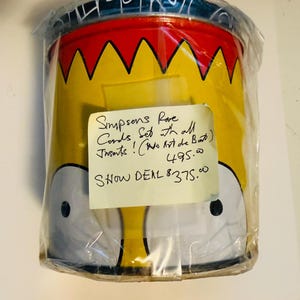 May include: A white ceramic mug with a black handle and the text "But First, Coffee" in a black, handwritten-style font. The mug is on a white surface.