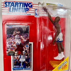 May include: A Starting Lineup Sports Superstar Collectibles action figure of Shaquille O'Neal in his Orlando Magic uniform. The figure is posed in a slam dunk position. The packaging includes a trading card of Shaquille O'Neal.