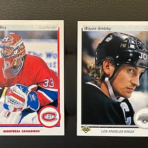 Może przedstawiać: Dwie karty kolekcjonerskie hokejowe, jedna z Patrickiem Royem, bramkarzem Montreal Canadiens, a druga z Wayne'em Gretzkym, środkowym Los Angeles Kings.