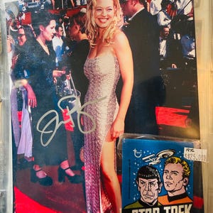 Può includere: Fotografia di una donna in un abito scintillante su un tappeto rosso. È visibile una carta collezionabile vintage di Star Trek. La carta presenta Spock e il Capitano Kirk, con il testo "STAR TREK" e "WITH 1 STICK BUBBLE GUM".