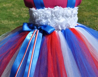 May include: A red, white, and blue tulle tutu with a white rosette bodice and blue ribbon sash. The tutu is perfect for a patriotic celebration.