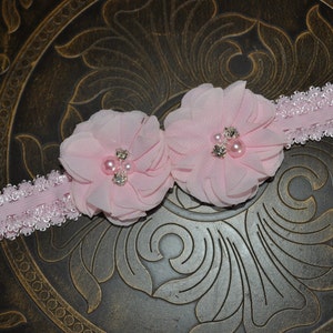 May include: A pink headband with two pink fabric flowers and pearl embellishments.