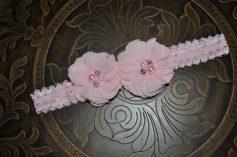May include: A pink headband with two pink fabric flowers and pearl embellishments.