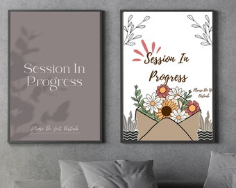 May include: Two framed signs with the text "Session In Progress" and a floral design. The sign on the left has a gray background and the sign on the right has a white background with a brown envelope and flowers.