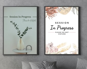 May include: Two framed signs with the text "Session In Progress - Please do not disturb" in black text on a white background. The sign on the left has a vase with green eucalyptus branches on a small table. The sign on the right has a floral design with beige and pink flowers and leaves.