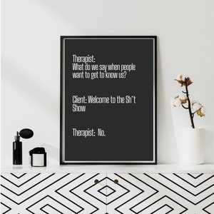 May include: A black and white framed print with a humorous conversation between a therapist and a client. The text reads: "Therapist: What do we say when people want to get to know us? Client: Welcome to the Sh*t Show Therapist: No."