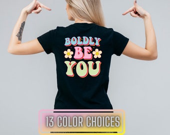 May include: Black t-shirt featuring a retro-style graphic that reads "BOLDLY BE YOU" in colourful letters with flowers and smiley faces.