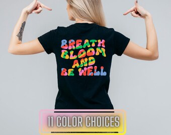 May include: Black t-shirt with the text "Breath Bloom And Be Well" in colourful, bubble-like letters.