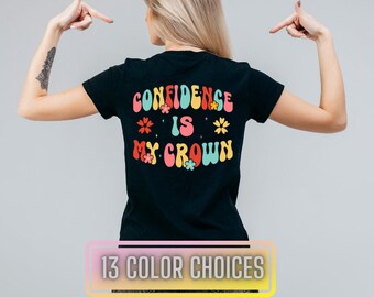 May include: Black t-shirt with the text "CONFIDENCE IS MY CROWN" in a retro font with colourful flowers.