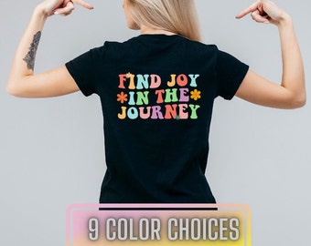 May include: Black t-shirt with a colourful graphic that says "Find Joy *in the* Journey" with flowers around the text.