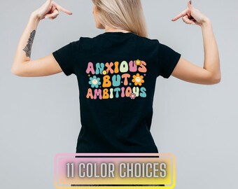 May include: Black t-shirt with the text "Anxious But Ambitious" in colourful, retro-style lettering with flower accents.