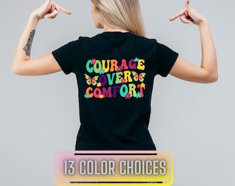 May include: Black t-shirt with the text "COURAGE OVER COMFORT" in colourful, retro-style letters with butterflies and flowers. 13 colour choices.