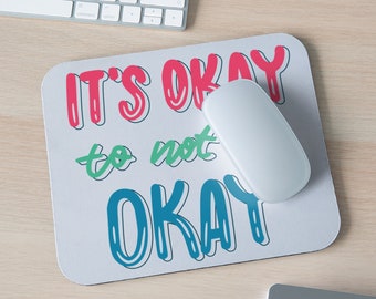 May include: A white mouse pad with the text "IT'S OKAY to not OKAY" in colorful, outlined letters. The text is in a playful, handwritten style.