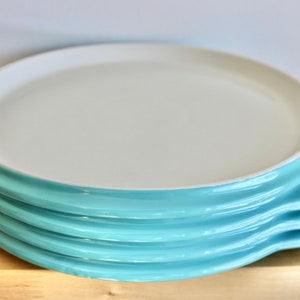 Peut inclure: Une pile de quatre assiettes en céramique turquoise et blanche avec un bord arrondi. Les assiettes sont empilées sur une surface en bois.