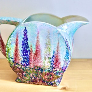 May include: A blue and green ceramic jug with a floral design. The jug has a rounded body and a wide spout. The floral design features pink, purple, and green flowers.