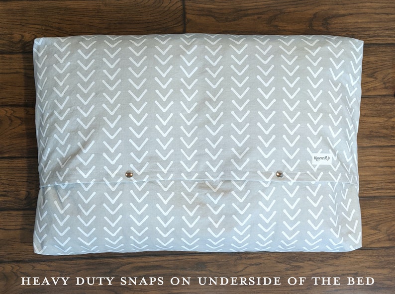 May include: A gray and white chevron patterned dog bed with heavy duty snaps on the underside. The bed has a white label with the word "remarkably" printed on it.
