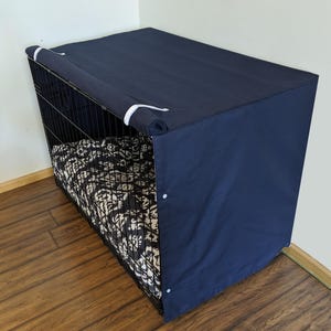 May include: A navy blue dog crate cover with a white trim. The cover is made of a soft, durable fabric and has a zippered opening for easy access. The cover is designed to provide privacy and a sense of security for your pet.