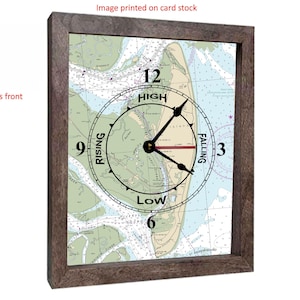 May include: A framed wall clock with a nautical chart design. The clock face features a tide chart with the words "High," "Low," "Rising," and "Falling." The clock hands are black, and the frame is a dark brown color. The image is printed on card stock.