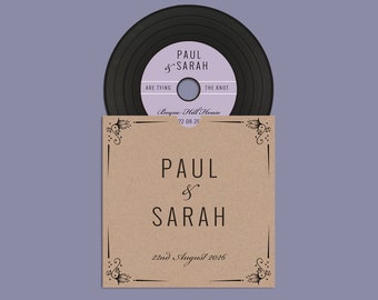 Könnte beinhalten: Eine braune Papier-Plattenhülle mit einer schwarzen Schallplatte darin. Die Hülle hat einen schwarzen Rand und florale Designs oben und unten. Der Text auf der Hülle lautet "Paul & Sarah" und "22nd August 2026". Der Text auf der Schallplatte lautet "Paul & Sarah are tying the knot" und "Boyne Hill House 22-08-26".