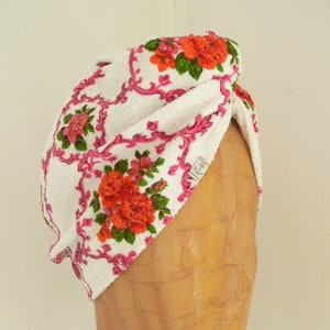 Op de afbeelding: Witte turban met een roze en groen bloemenpatroon. De turban is gemaakt van zacht badstof.