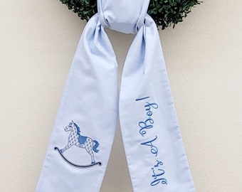May include: A light blue fabric ribbon with a rocking horse embroidered on one side and the text "It's a Boy!" embroidered on the other side.