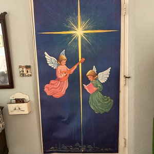 May include: A vintage Christmas door decoration featuring two angels, one playing a lute and the other holding a book, against a blue starry night sky with a bright yellow star.