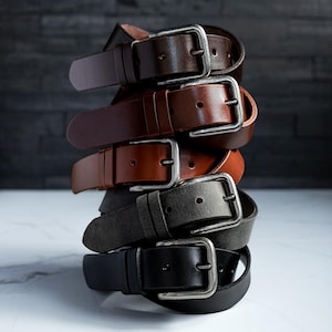 May include: A stack of five leather belts in different colors, including brown, tan, gray, and black. Each belt has a silver buckle.