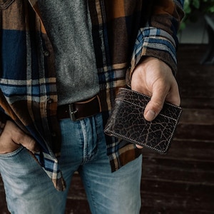 May include: A brown leather wallet with a textured surface. The wallet is being held in a person's hand.