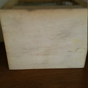 Pode incluir: Uma caixa de madeira branca com uma tampa de madeira natural. A caixa est&aacute; vazia e tem um aspecto r&uacute;stico.