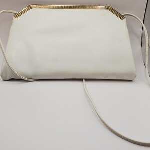 May include: A white leather clutch purse with a gold metal frame and a long white strap.