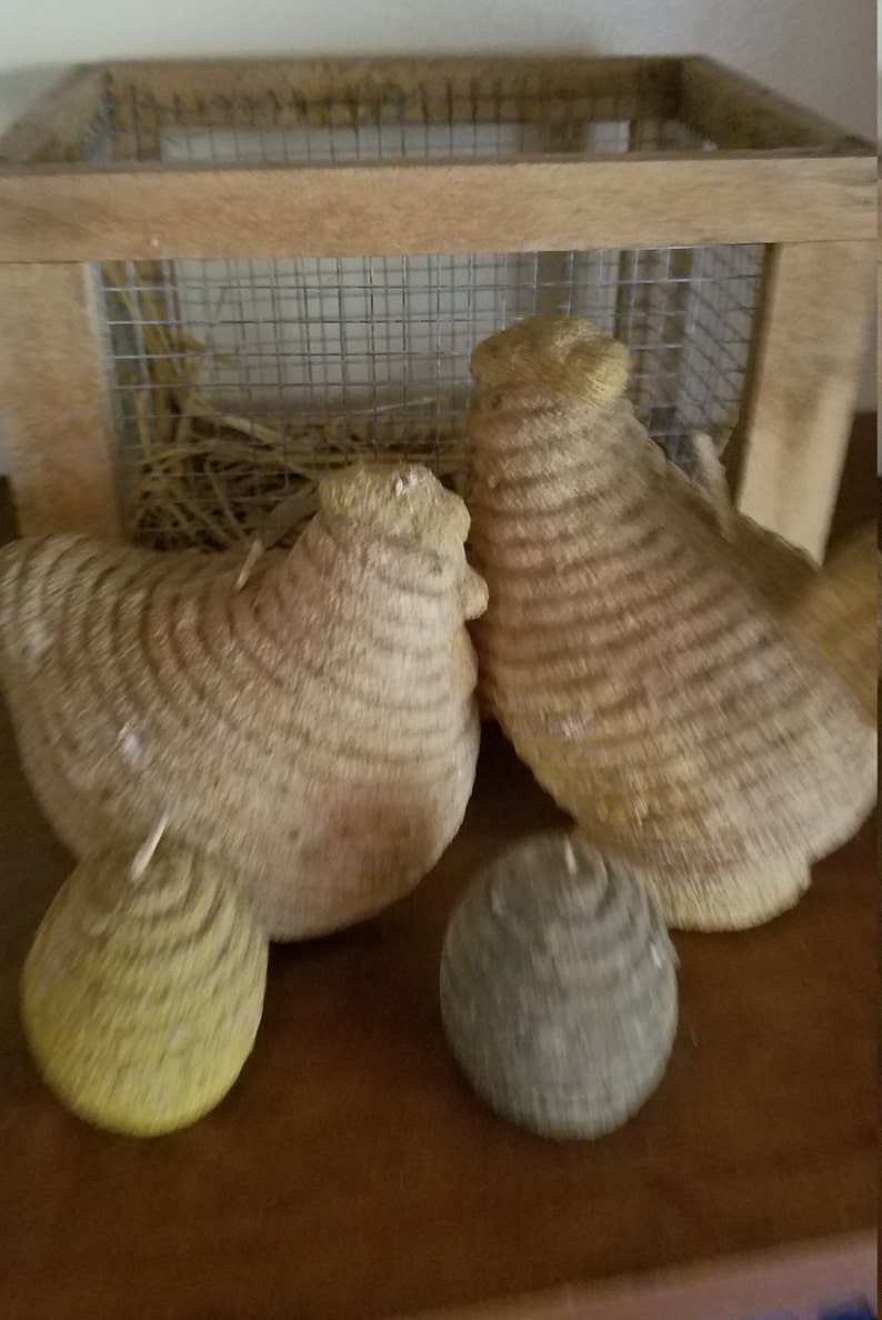 Pode incluir: Dois frangos tecidos de palha e uma bola redonda tecida de palha, todos sentados em uma superf&iacute;cie de madeira. Os frangos est&atilde;o em frente a uma gaiola de madeira com uma malha de arame.