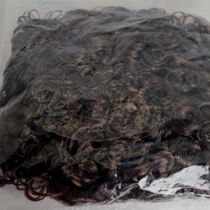 May include: A close-up of a brown curly wig in a plastic bag.