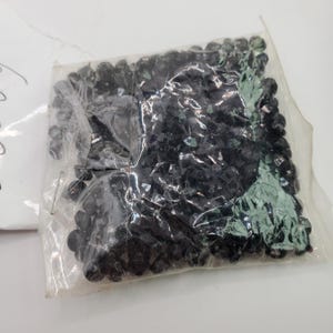 May include: A clear plastic bag filled with black glass beads. The beads are small and round, and they are ideal for crafting or decorating.