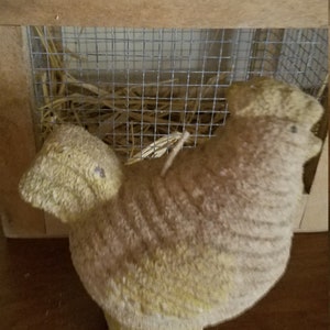 Pode incluir: Uma vela em forma de frango amarela e marrom, sentada dentro de uma gaiola de madeira com um ninho de palha.