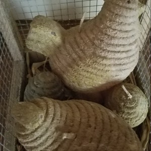 Pode incluir: Tr&ecirc;s figuras de frango de cer&acirc;mica marrom com um padr&atilde;o texturizado e tecido. Os frangos est&atilde;o em uma gaiola de arame com palha no fundo.