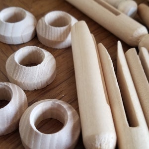 May include: A close-up of wooden craft supplies, including dowels, clothespins, and wooden rings. The wood is a natural light brown color.