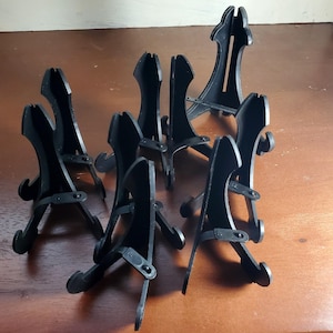 May include: A set of eight black plastic display stands for showcasing small items like figurines, plates, or other collectibles. The stands are made of sturdy plastic and have a simple, elegant design.