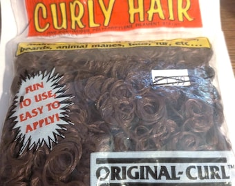 May include: A clear plastic bag containing brown curly hair, a continuous polypropylene filament strand. The packaging features the text "CURLY HAIR", "ORIGINAL-CURL", "FUN TO USE EASY TO APPLY", and "beards, animal manes, toys, fur, etc..." with illustrations.