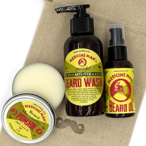 May include: A set of beard care products in a brown canvas bag. The set includes a brown bottle of beard wash, a brown bottle of beard oil, and a silver tin of beard pomade. The labels on the bottles and tin feature a red and yellow logo with the text "Medicine Man's" and the product name. The beard wash bottle has the text "powerful anti-itch" and the beard oil bottle has the text "Beard Oil". The beard pomade tin has the text "Beard Moustache Pomade".
