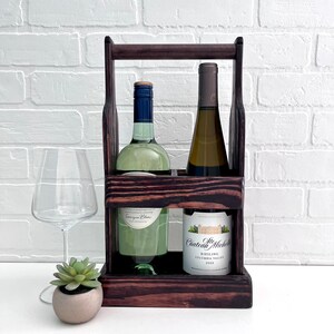 May include: A dark brown wooden wine carrier with two bottles of white wine. The carrier has a handle on the top and two compartments for bottles. The bottles are labeled "Chateau Michelle" and "Seventeen Palms".