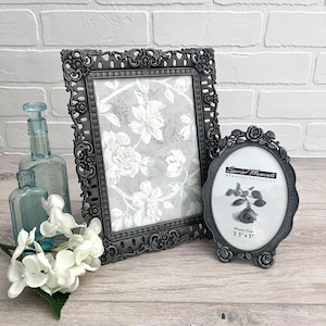 May include: Two ornate, dark gray picture frames, one rectangular and one oval, with floral details. The rectangular frame holds a floral print. The oval frame has the text "Special Moments" and a photo size of 3.5" x 5".