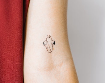 Puede incluir: Un dibujo simple de un fantasma con una cara sonriente, tatuado en el brazo de una persona.